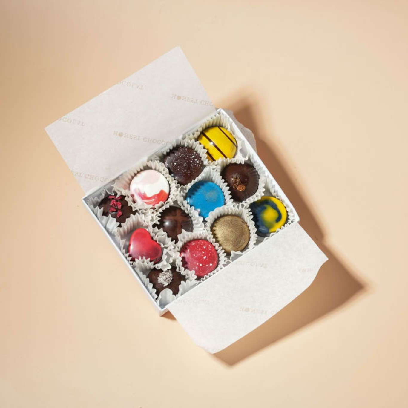 Assorted colorful chocolates in an open box on a beige background