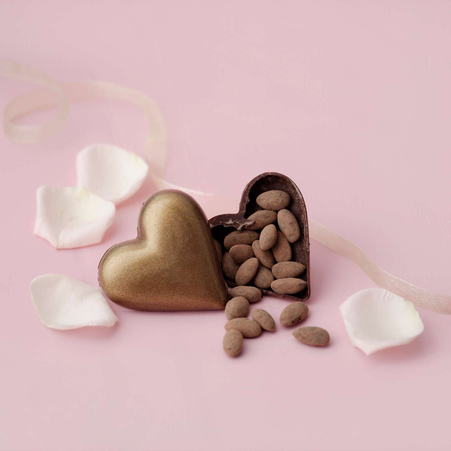 Heart-shaped chocolate box with almonds on a pink background